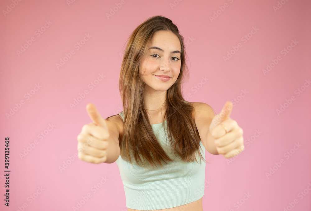 Happy female college student showing thumbs up over pink background Happy female college student showing thumbs up over pink background