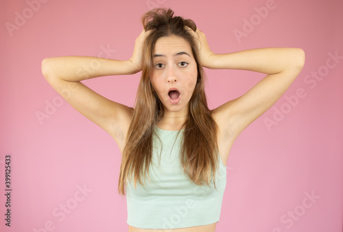 Young beautiful woman with straw hat feeling horrified and shocked  raising hands to head and panicking at a mistake against pink wall