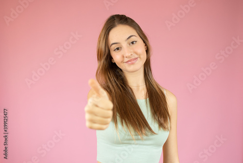 Happy female college student showing thumbs up over pink background