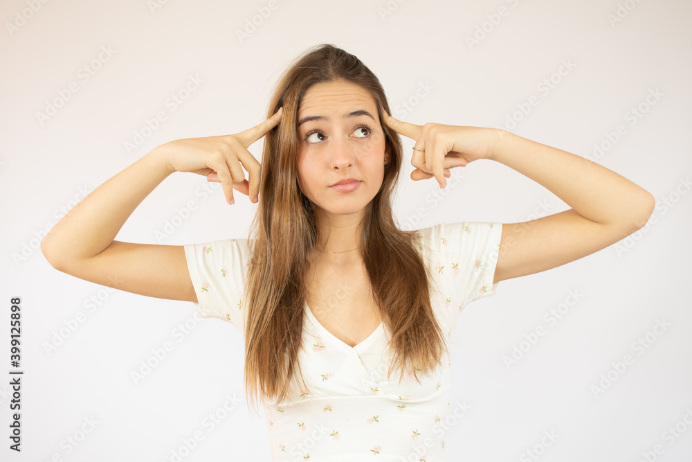 Young beautiful woman over isolated white background and thinking with two fingers on her head very concentrated. Young beautiful woman over isolated white background and thinking with two fingers on her head very concentrated.