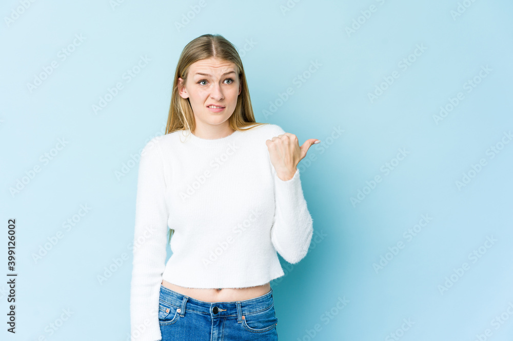 Young blonde woman isolated on blue background shocked pointing with index fingers to a copy space. Young blonde woman isolated on blue background shocked pointing with index fingers to a copy space.