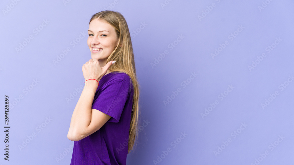 Young blonde woman isolated on purple background points with thumb finger away, laughing and carefree. Young blonde woman isolated on purple background points with thumb finger away, laughing and carefree.