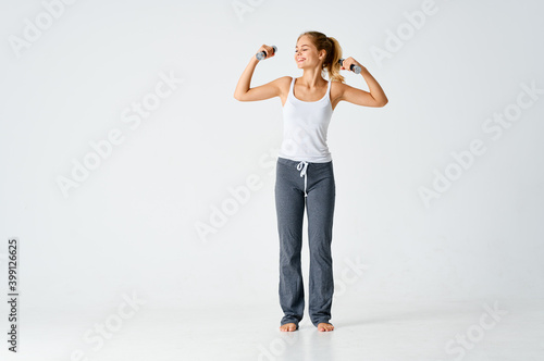 sports woman with dumbbells in her hands on a light background in full growth 