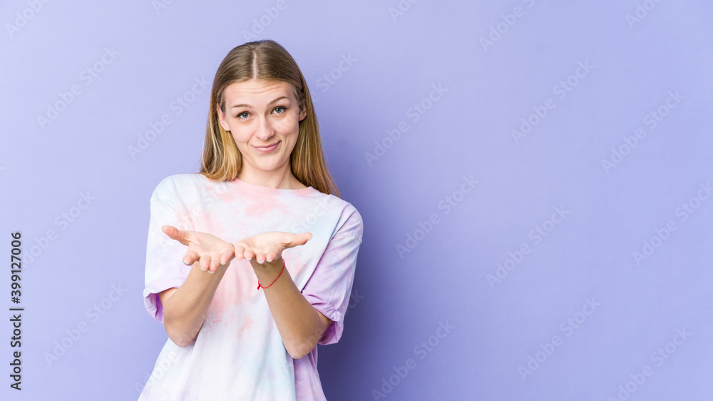 Young blonde woman isolated on purple background holding something with palms, offering to camera. Young blonde woman isolated on purple background holding something with palms, offering to camera.