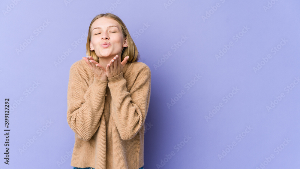Young blonde woman isolated on purple background folding lips and holding palms to send air kiss. Young blonde woman isolated on purple background folding lips and holding palms to send air kiss.
