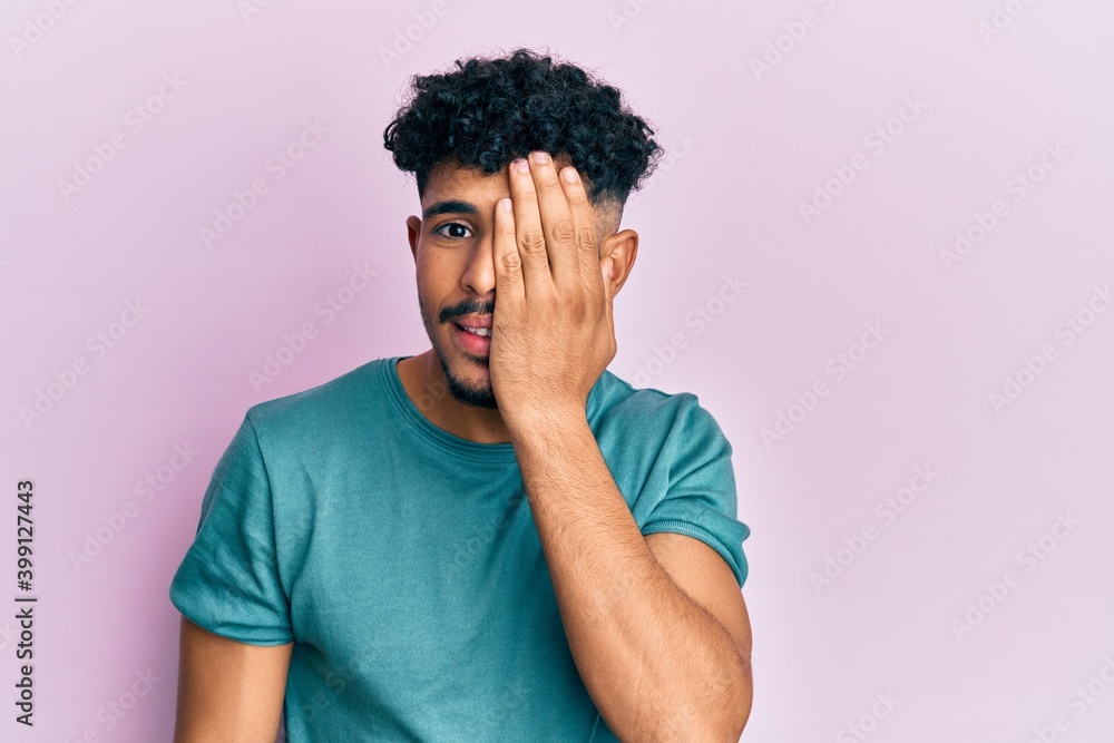 Young arab handsome man wearing casual clothes covering one eye with hand, confident smile on face and surprise emotion. Young arab handsome man wearing casual clothes covering one eye with hand, confident smile on face and surprise emotion.