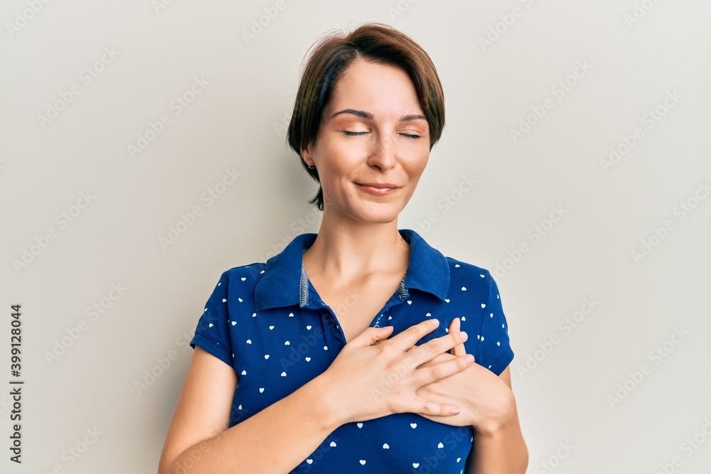Young brunette woman with short hair wearing casual clothes smiling with hands on chest, eyes closed with grateful gesture on face. health concept. Young brunette woman with short hair wearing casual clothes smiling with hands on chest, eyes closed with grateful gesture on face. health concept.