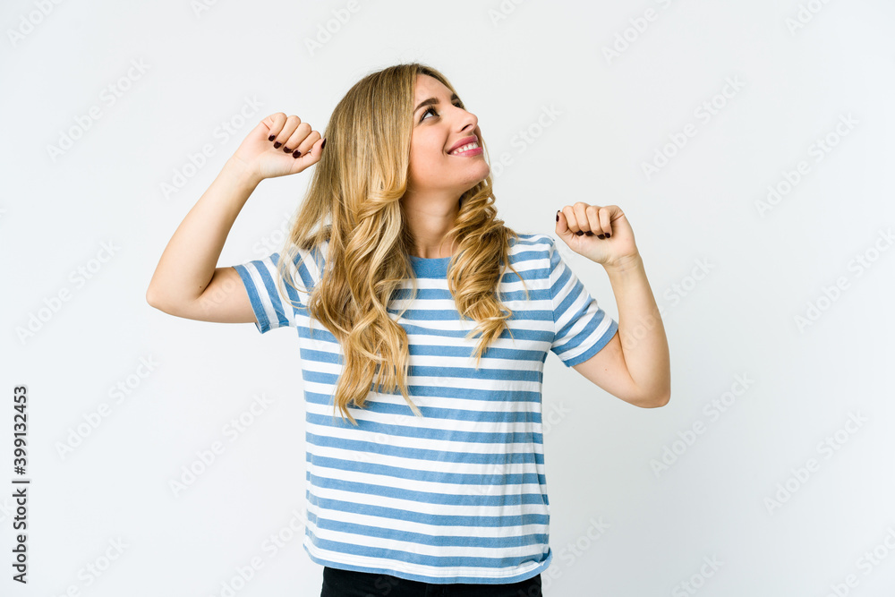 Young caucasian blonde woman celebrating a special day, jumps and raise arms with energy.
