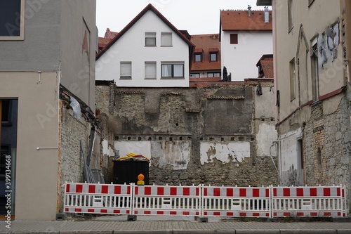 A construction site among houses in the street. It is secured with red and white plastic barrier panels. A scene from the city center of city Constance in Germany.