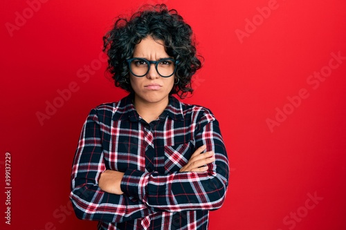 Young hispanic woman with curly hair wearing casual clothes and glasses skeptic and nervous, disapproving expression on face with crossed arms. negative person.