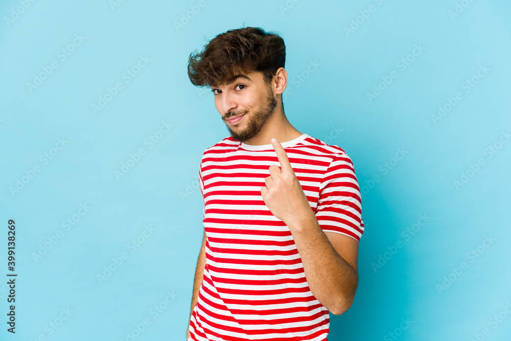 Young arab man on blue background pointing with finger at you as if inviting come closer. Young arab man on blue background pointing with finger at you as if inviting come closer.