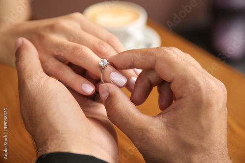 Man putting engagement ring on his girlfriend s finger in cafe  closeup