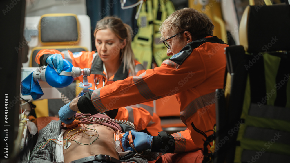 EMS Paramedics Team Provide Medical Help to Injured Patient on the Way to Hospital. Emergency Care Assistants Using a Defibrillator and Ventilation Mask to Bring the Man Back to Life in an Ambulance. EMS Paramedics Team Provide Medical Help to Injured Patient on the Way to Hospital. Emergency Care Assistants Using a Defibrillator and Ventilation Mask to Bring the Man Back to Life in an Ambulance.