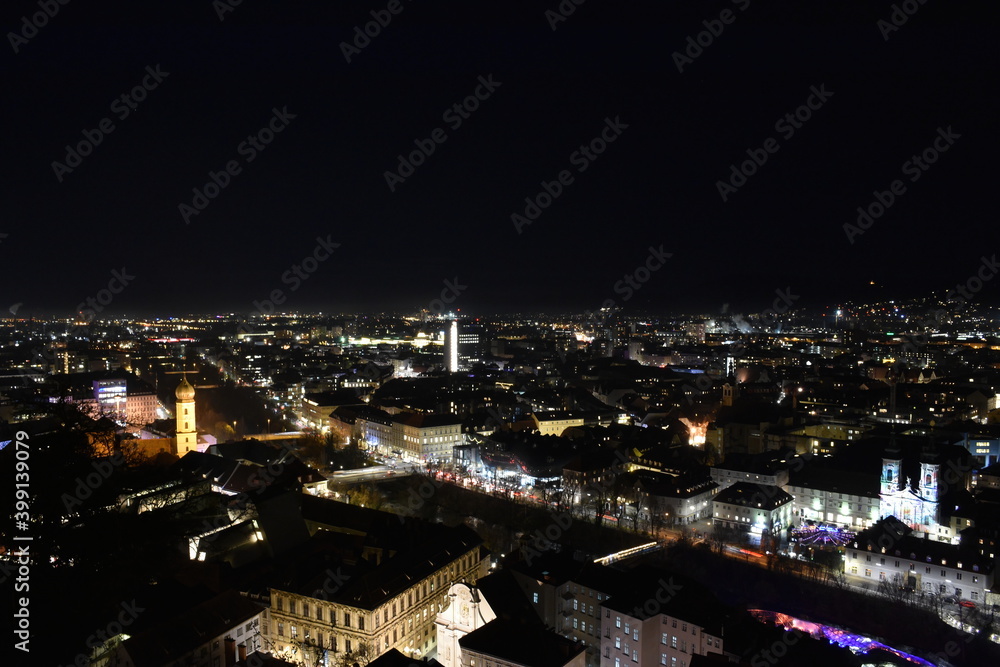 City lights of Graz and the famous clock tower (Grazer Uhrturm) on Shlossberg hill, Graz, Styria region, Austria, by night. Panoramic view.