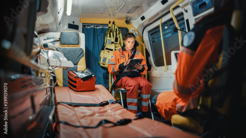 Professional Female EMS Paramedic Using Tablet Computer while Riding in an Ambulance Vehicle for an Emergency. Emergency Medical Technicians are on Their Way to a Call Outside the Healthcare Hospital.