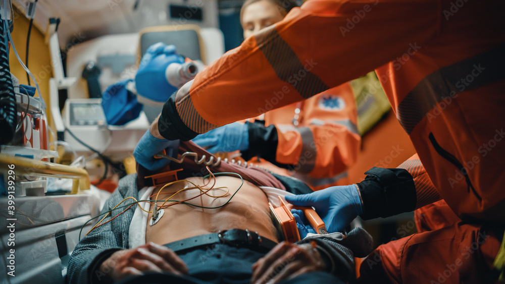 Female and Male EMS Paramedics Provide Medical Help to an Injured Patient on the Way to a Healthcare Hospital. Emergency Care Assistants Putting On Non-Invasive Ventilation Mask in an Ambulance. Female and Male EMS Paramedics Provide Medical Help to an Injured Patient on the Way to a Healthcare Hospital. Emergency Care Assistants Putting On Non-Invasive Ventilation Mask in an Ambulance.