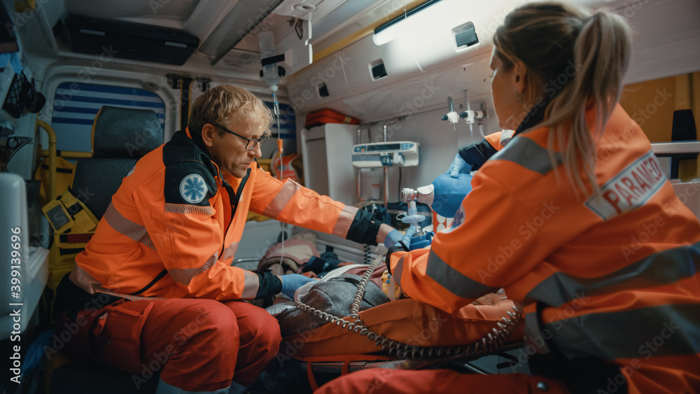 EMS Paramedics Team Provide Medical Help to Injured Patient on the Way to Hospital. Emergency Care Assistants Using a Defibrillator and Ventilation Mask to Bring the Man Back to Life in an Ambulance. EMS Paramedics Team Provide Medical Help to Injured Patient on the Way to Hospital. Emergency Care Assistants Using a Defibrillator and Ventilation Mask to Bring the Man Back to Life in an Ambulance.