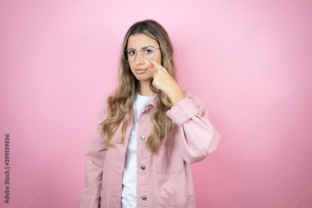 Young beautiful blonde woman with long hair standing over pink background Pointing to the eye watching you gesture, suspicious expression Young beautiful blonde woman with long hair standing over pink background Pointing to the eye watching you gesture, suspicious expression