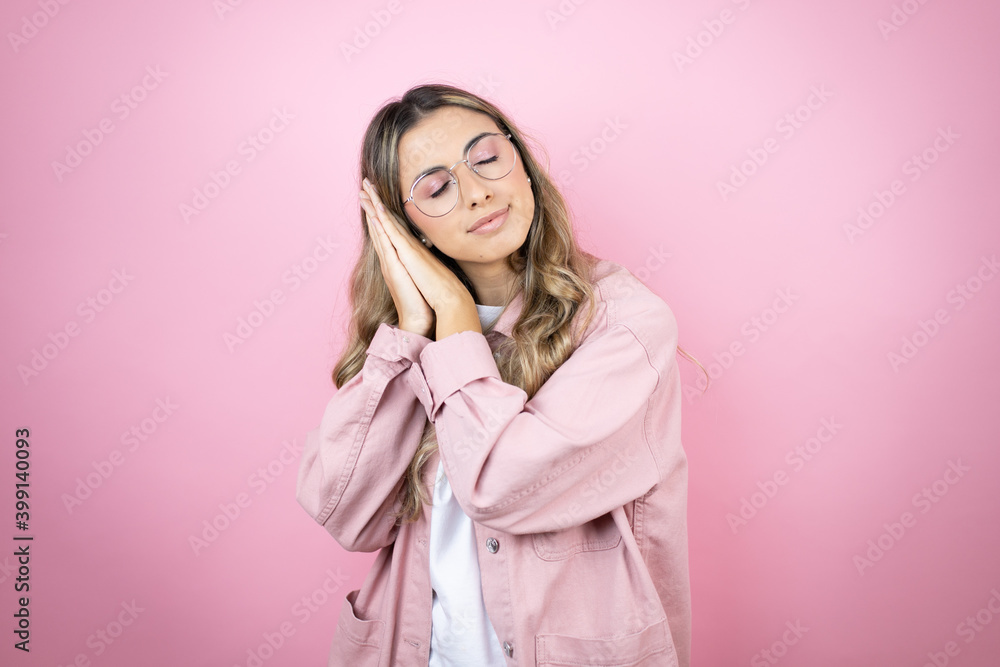 Young beautiful blonde woman with long hair standing over pink background sleeping tired dreaming and posing with hands together while smiling with closed eyes. Young beautiful blonde woman with long hair standing over pink background sleeping tired dreaming and posing with hands together while smiling with closed eyes.