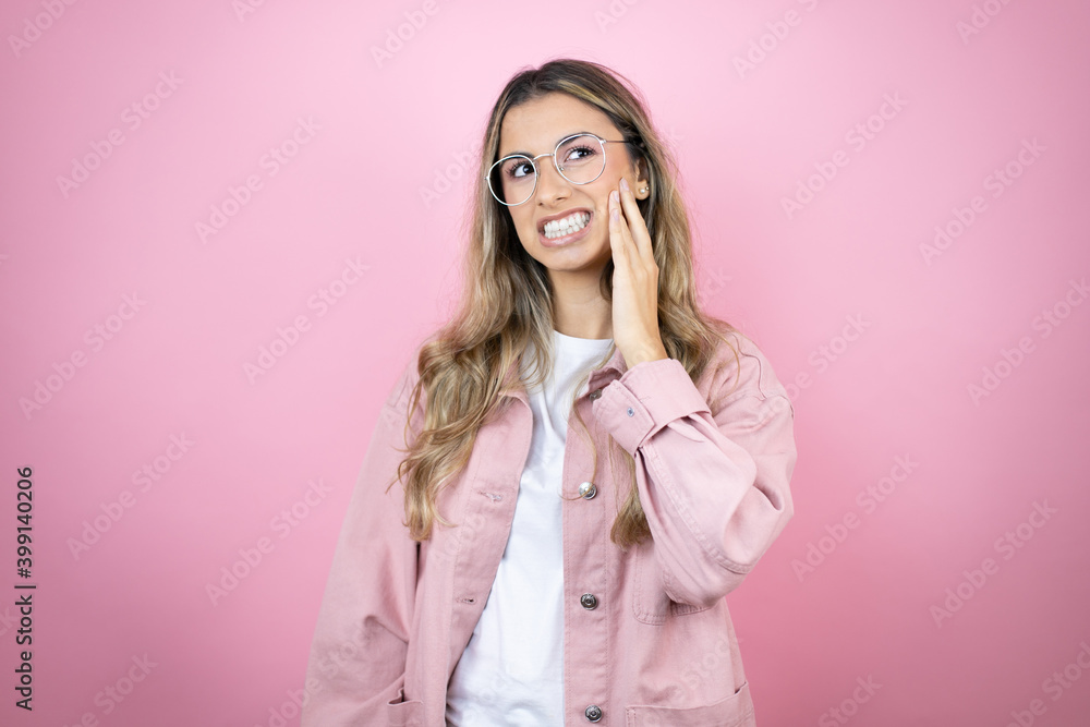 Young beautiful blonde woman with long hair standing over pink background touching mouth with hand with painful expression because of toothache or dental illness on teeth Young beautiful blonde woman with long hair standing over pink background touching mouth with hand with painful expression because of toothache or dental illness on teeth