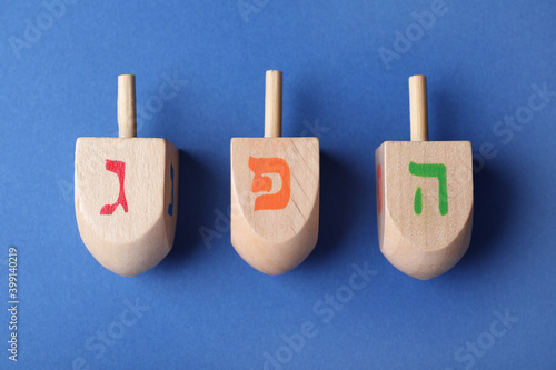 Hanukkah traditional dreidels with letters Gimel, He and Pe on blue background, flat lay photo