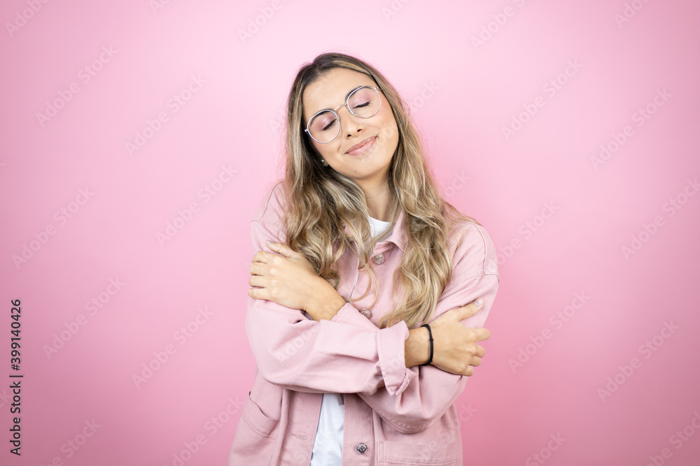 Young beautiful blonde woman with long hair standing over pink background hugging oneself happy and positive, smiling confident Young beautiful blonde woman with long hair standing over pink background hugging oneself happy and positive, smiling confident