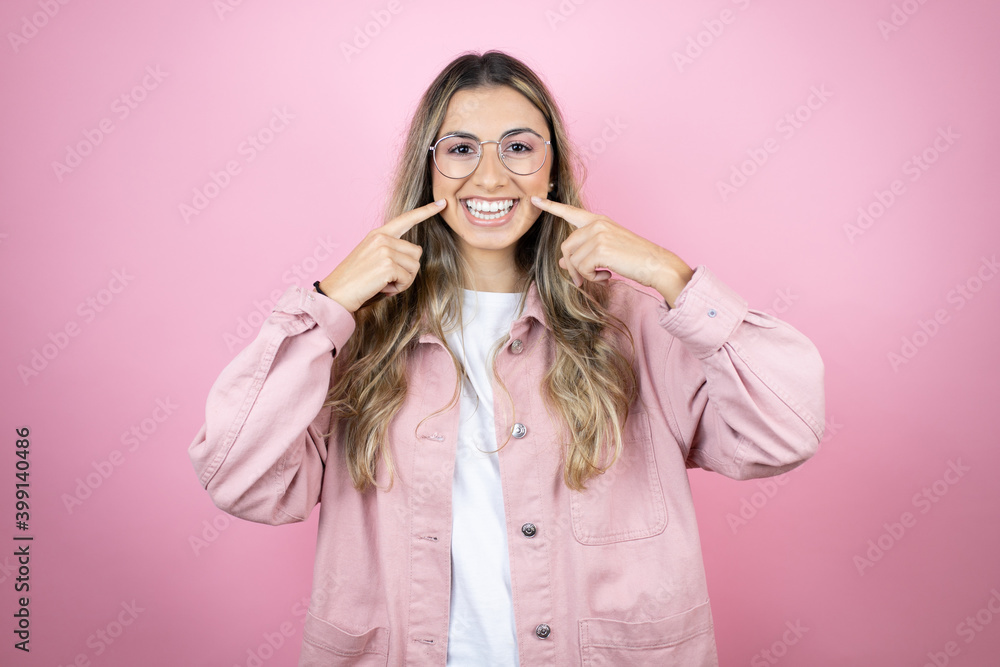 Young beautiful blonde woman with long hair standing over pink background smiling confident showing and pointing with fingers teeth and mouth Young beautiful blonde woman with long hair standing over pink background smiling confident showing and pointing with fingers teeth and mouth
