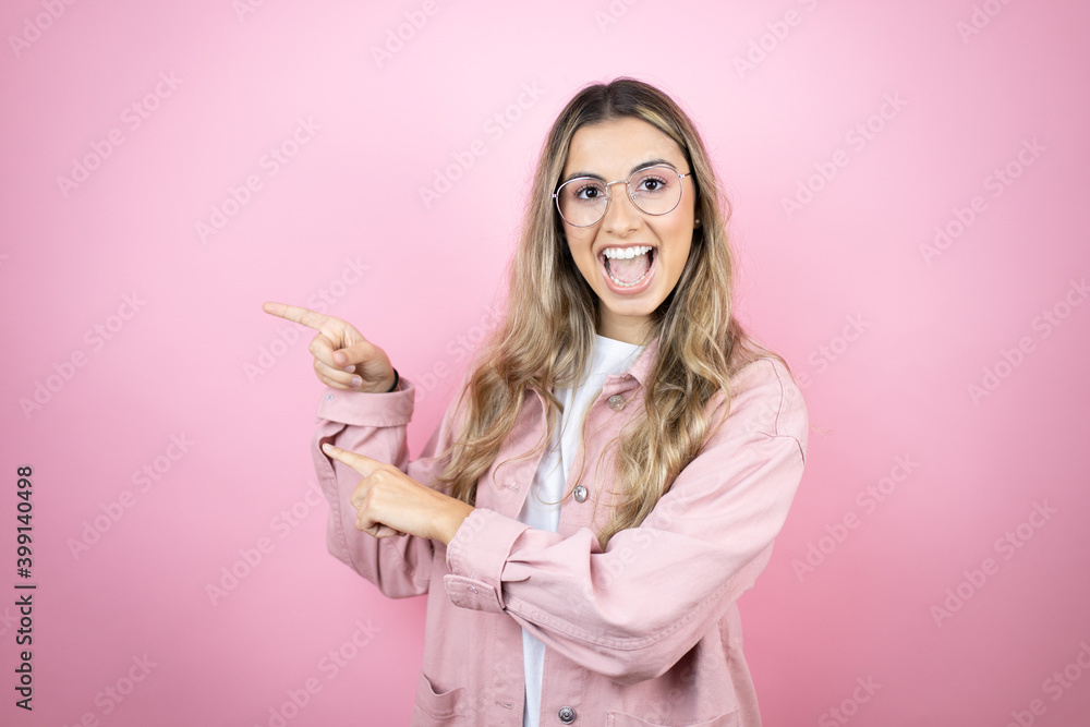 Young beautiful blonde woman with long hair standing over pink background pointing to the copy space on the side with both hands Young beautiful blonde woman with long hair standing over pink background pointing to the copy space on the side with both hands