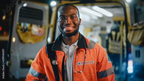 Portrait of a Black African American EMS Paramedic Proudly Standing in Front of Camera in High Visibility Medical Orange Uniform and Smiling. Successful Emergency Medical Technician or Doctor at Work. photo