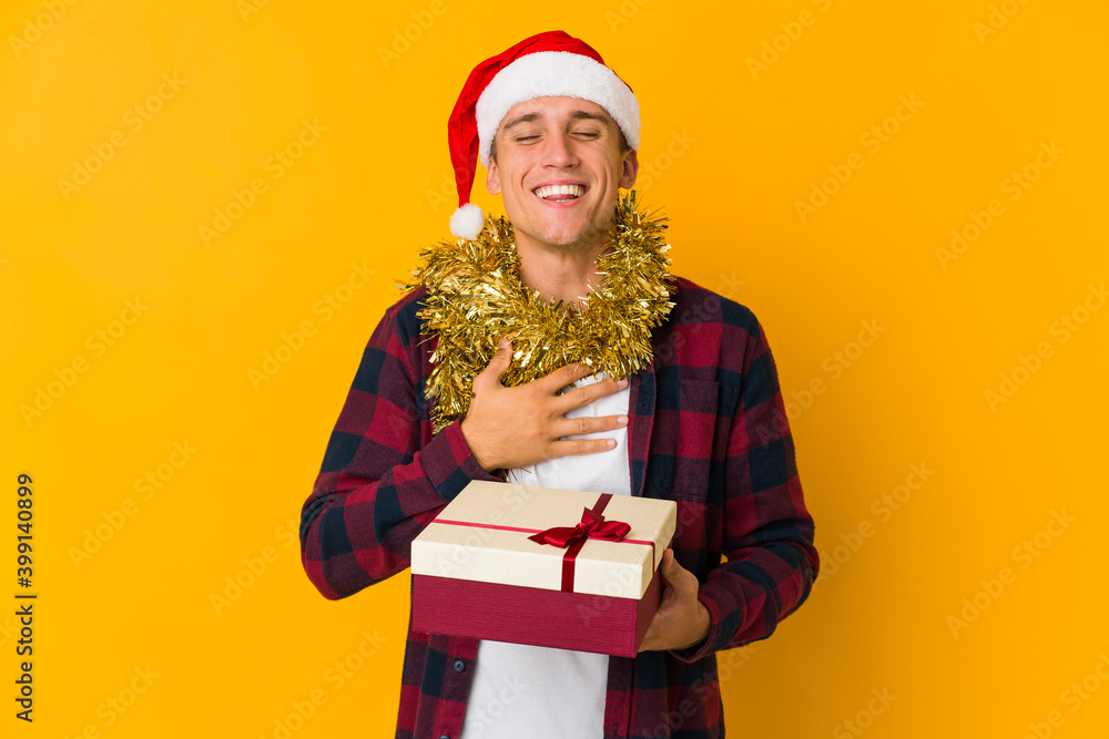 Young caucasian man with christmas hat holding a present isolated on yellow background Young caucasian man with christmas hat holding a present isolated on yellow background