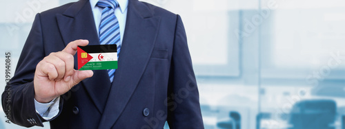 Cropped image of businessman holding plastic credit card with printed flag of Western Sahara. Background blurred. photo