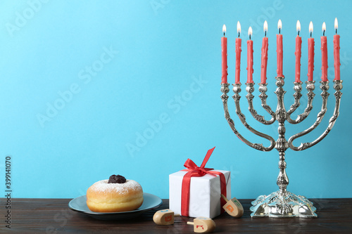 Silver menorah near dreidels with He, Pe, Nun, Gimel letters, gift box and sufganiyah on wooden table, space for text. Hanukkah symbols
