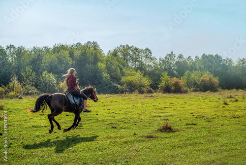 Young woman riding a horse at a gallop - near the Black Sea coast . She is instructor of group of  riders Variant:  Girl riding instructor galloping on the lawn on a sunny day.   © Marat Lala
