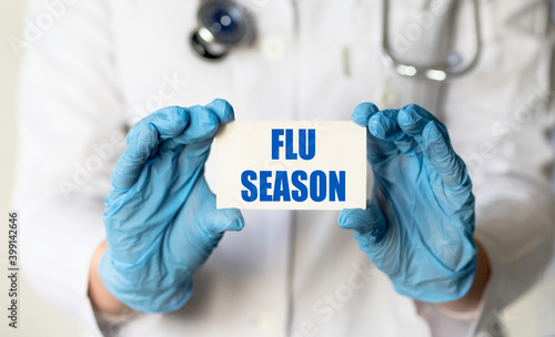 A medical worker in gloves holds a card with the words FLU SEASON. Medical concept.
