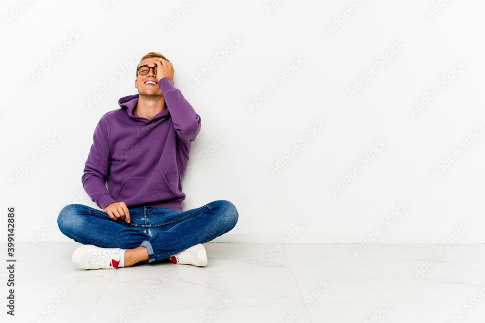 Young caucasian man sitting on the floor laughing happy, carefree, natural emotion.