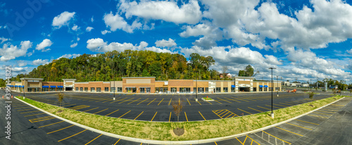 Panoramic view of refurbished American suburban strip mall with no logo or signage, covered with brick veneer, around an empty newly surfaced and painted parking lot with dramatic cloudy blue sky photo