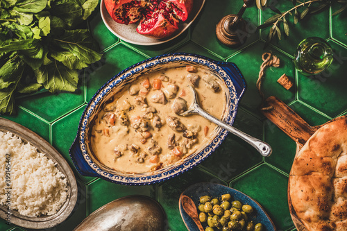 Turkish style family dinner concept. Flat-lay of stewed lamb in yogurt sauce, rice pilav, flatbread and ingredients for salad over green table, top view. Ramazan iftar, gathering, celebration supper