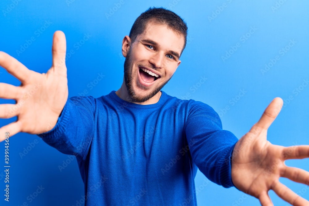 Young handsome man wearing casual sweater looking at the camera smiling with open arms for hug. cheerful expression embracing happiness. Young handsome man wearing casual sweater looking at the camera smiling with open arms for hug. cheerful expression embracing happiness.