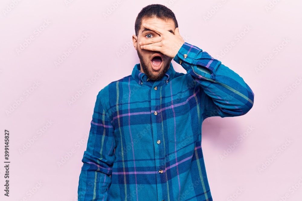 Young handsome man wearing casual shirt peeking in shock covering face and eyes with hand, looking through fingers afraid Young handsome man wearing casual shirt peeking in shock covering face and eyes with hand, looking through fingers afraid