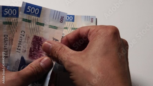 Unas manos cuentan billetes de 500 y de 200 pesos mexicanos frente a la cámara sobre una mesa blanca