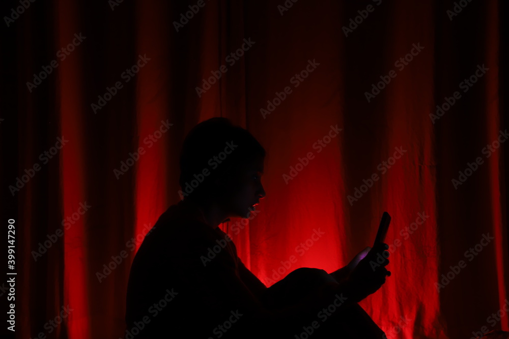 silhouette of a person in a red curtain with a mobile phone -a conceptual photograph of the modren era