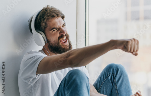 emotional man listening to music on headphones and gesturing with his hands near the window
