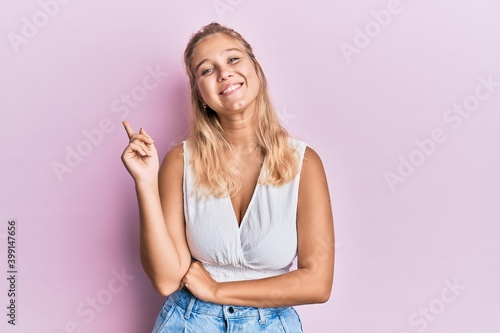 Young blonde girl wearing casual clothes with a big smile on face, pointing with hand and finger to the side looking at the camera. © Krakenimages.com