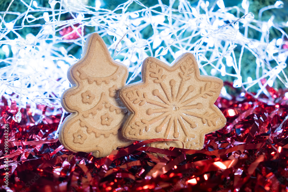 Close-up of gingerbread christmas tree and snowflake on festive New Year background. Red tinsel and garland on backdrop.