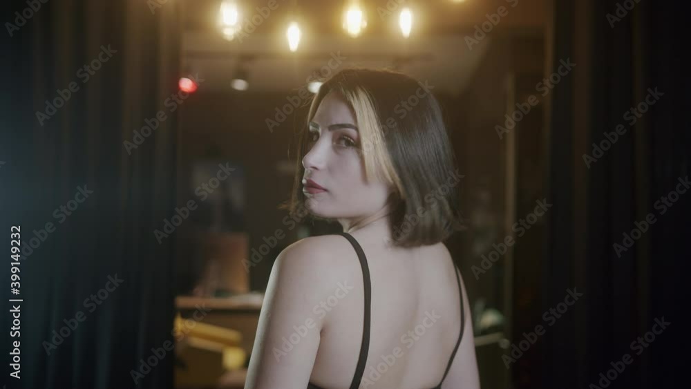 Young beautiful and attractive woman with short hair in a black dress turns her back and poses for the camera. Cinematic 4K close-up Young beautiful and attractive woman with short hair in a black dress turns her back and poses for the camera. Cinematic 4K close-up