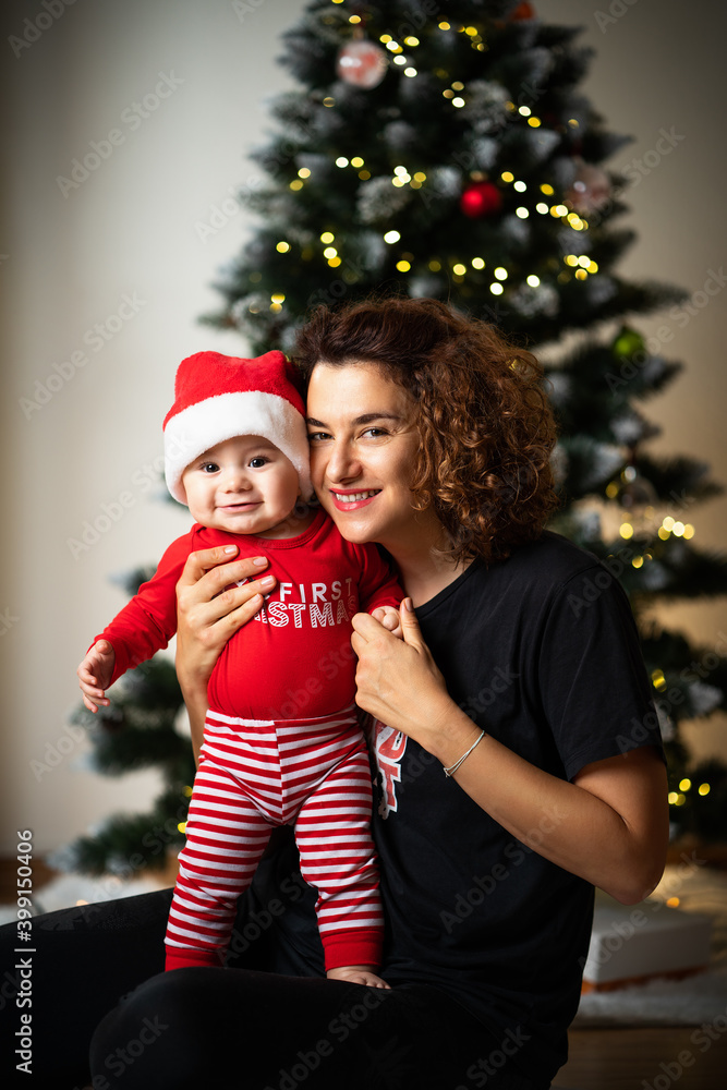smiling mother with a baby boy in a Christmas outfit in front of a Christmas tree smiling mother with a baby boy in a Christmas outfit in front of a Christmas tree