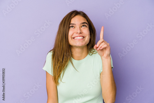 Young skinny caucasian girl teenager on purple background indicates with both fore fingers up showing a blank space.