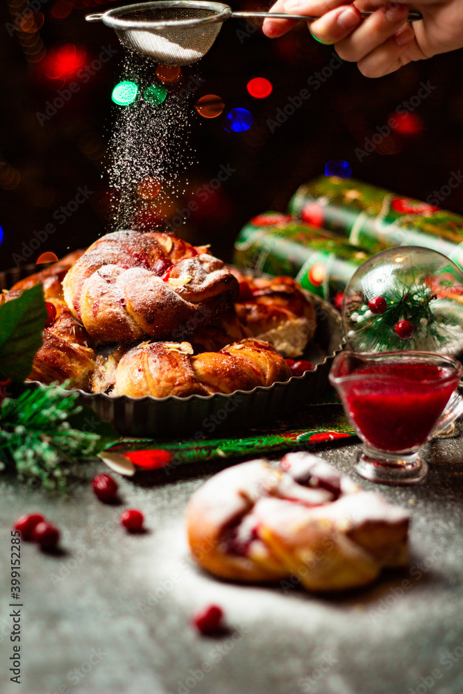 Tasty homemade braided buns with cranberry jam and sugar powder. Christmas and New Year decorations. Snow imitation. Bokeh lights background. Vertical orientation