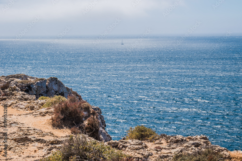Hiking up the cliff by the Atlantic Ocean with the silhouette of a sailing boat on the horizon of the Portuguese coast