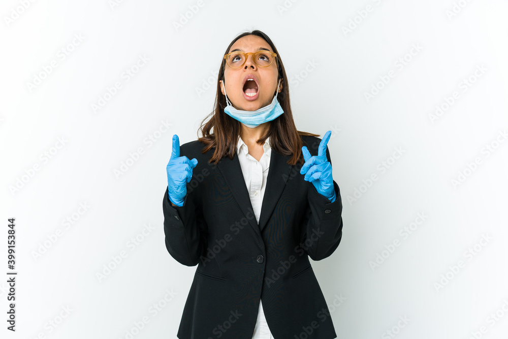 Young business latin woman wearing a mask to protect from covid isolated on white background pointing upside with opened mouth. Young business latin woman wearing a mask to protect from covid isolated on white background pointing upside with opened mouth.